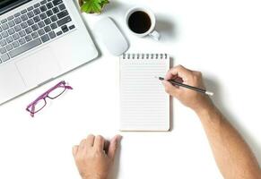 White office desk table with hand man writing on blank notebook photo