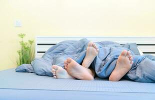 Two pairs of feet of kids under blanket in bed, photo