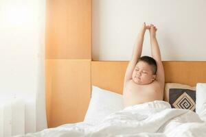 obeso grasa chico despierta arriba y extensión en cama en Mañana foto
