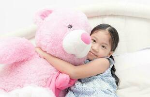 linda asiático pequeño niña abrazando grande rosado oso foto