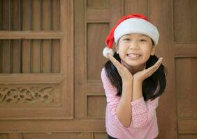 Cute asian girl wearing santa hat smile on old wood wall background, photo
