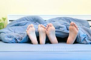 Two pairs of feet of kids. Brother and sister lying under blanket photo