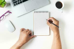 White office desk table with hand man writing on blank notebook photo