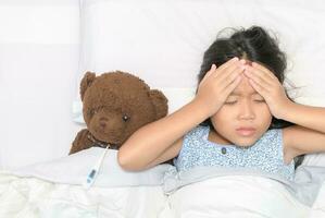 enfermo niño. asiático pequeño niña dolor de cabeza y acostado en cama, foto