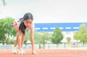 alegre linda niña en Listo posición a correr en pista, foto