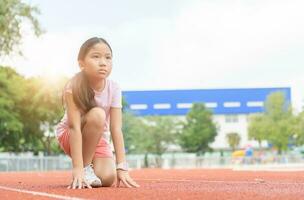 alegre linda niña en Listo posición a correr en pista, foto