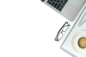 Desk with laptop, eye glasses, notebook and a cup of coffee isolated photo