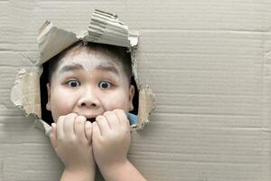 boy looking through hole on cardboard with shocked face photo