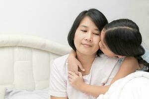 Daughter kissing her mother on bed, photo