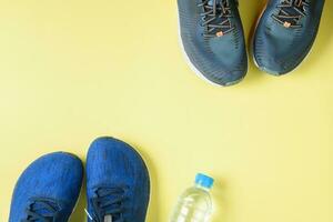 Two running shoes and bottle of water on yellow background, photo