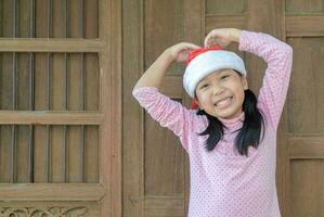 Cute asian girl wearing santa hat smile on old wood wall photo