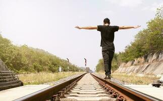 Man wearing black shirt spreads his hands and balances on train tracks photo