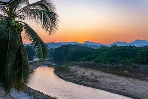 puesta de sol sobre las montañas con río y palmera foto