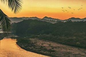 puesta de sol sobre las montañas con río y palmera foto