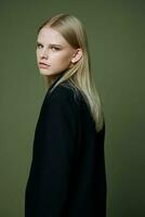 A close portrait of a blonde looking over her shoulder in a black jacket posing in a studio on a green background. The concept of stylish fashion photography photo