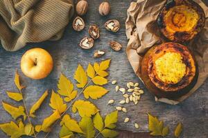 Millet porridge baked in pumpkin, walnut, seeds, apple, yellow leaves, warm sweater on an old wooden background. Toned image. Top view. photo