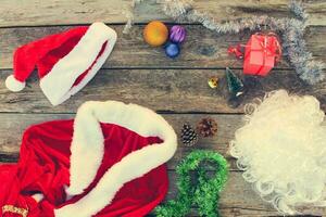 Santa Claus suit, small tree, pinecone, Christmas balls, garland, gift on wooden background. Top view. Toned image. photo