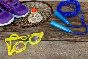 Sports equipment the birdie is on the racket, skipping rope, swimming goggles and sneakers on wooden background photo