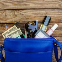 Things from open lady handbag. women's purse on wood background. Cosmetics, money and women's accessories fell out of the blue handbag. photo