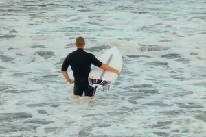 surfistas consiguiendo Listo a entrar el agua y caminando con el tablero a lo largo el costa. foto