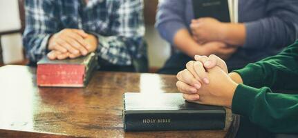 Small group of asian people praying worship believe. Teams of friends worship together before studying Holy bible. family praying together in church. Small group learning with prayer concept. photo