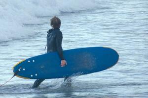 Surfers getting ready to enter the water and walking with the board along the shore. photo