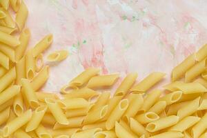 Raw Italian penne pasta on pink background photo