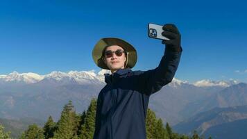 A young traveler takes a selfie or a video call while standing a top a mountain. photo