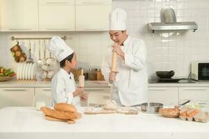 Young Asian father and his son wearing chef uniform baking together in kitchen at home photo