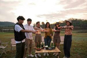 grupo de joven asiático personas son disfrutar cámping , jugando bengala en natural cámping a crepúsculo foto