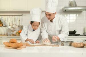 Young Asian father and his son wearing chef uniform baking together in kitchen at home photo