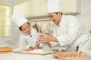 Young Asian father and his son wearing chef uniform baking together in kitchen at home photo