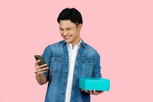 Portrait handsome Asian man in casual clothes with holding a box and happy using online shopping on smartphone photo