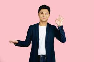 Handsome and friendly face asian businessman smile in formal gesture and showing hand ok on pink background studio shot. photo