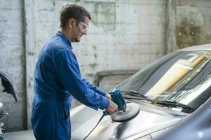 caucásico hombre es utilizando coche pulido máquina en reparar mecánico pintura tienda foto