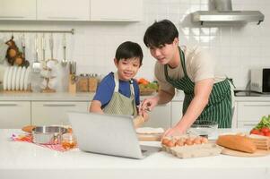 contento joven asiático padre y hijo haciendo desayuno juntos. juguetón en cocina a hogar foto