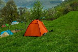 Camping tents on a green meadow in the mountains in spring. Rest with the tent in nature photo