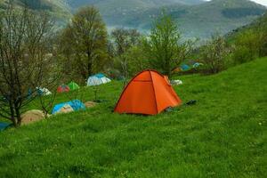 cámping carpas en un verde prado en el montañas en primavera. descanso con el tienda en naturaleza foto