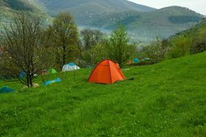 cámping carpas en un verde prado en el montañas en primavera. descanso con el tienda en naturaleza foto