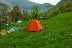 cámping carpas en un verde prado en el montañas en primavera. descanso con el tienda en naturaleza foto