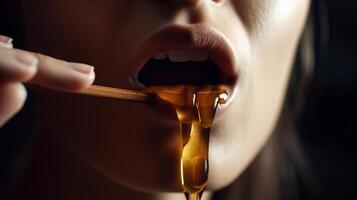 Honey dripping from honey dipper on girl lips. Beauty model woman open mouth, model eating nectar. Healthy food concept, diet, dessert, photo