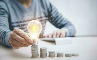 Businessman hand holding light bulb on coins stack on the wooden table , Saving ideas and investment budget, Creative ideas concept of saving money  concept, Copy space photo