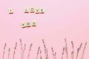 yo amor usted hecho de de madera letras en un rosado antecedentes con flores madres día tarjeta. plano laico para madres día foto