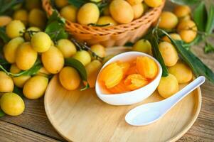 tropical fruit Name in Thailand sweet Yellow Marian Plum Maprang Plango or Mayong chid, Sweet dessert marian plum fruit  on bowl for food and wooden background photo