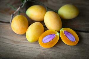 tropical fruit Name in Thailand Sweet Yellow Marian Plum Maprang Plango or Mayong chid, Marian plum fruit and leaves in plate on wooden background photo