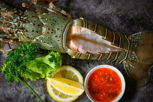 spiny lobster sashimi seafood, fresh lobster or rock lobster with herb and spices lemon parsley on dark background, raw spiny lobster for cooking food photo