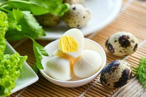 boiled eggs food, quail eggs on white bowl, breakfast eggs with fresh quail eggs and vegetable lettuce on table background photo