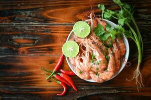 Fresh shrimps prawns seafood lemon lime with herbs and spice, shrimp on white bolw and wooden background dining table food photo