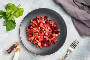 Vinaigrette with beetroot and boiled vegetables, traditional Russian homemade salad. A black plate on a light background. photo