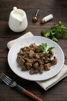 Fried or baked chicken liver with onion and sauce, green parsley leaves on a plate. Meat dish enriched with iron. photo